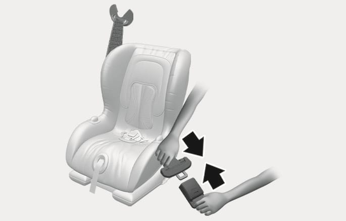 2025 Hyundai Tucson Child Restraint System installation image. Hands are shown fastening the seat belt through the child seat, with black arrows indicating the direction to insert the tongue and pull the strap to tighten. This explains the function of securing the child restraint system.