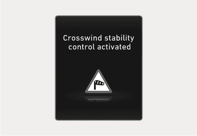 2025 Hyundai Tucson Crosswind Stability Control warning message image. The cluster display shows the text 'Crosswind stability control activated' above a triangular warning icon containing a windsock symbol. Explains the alert displayed when the system operates to stabilize the vehicle against strong crosswinds.