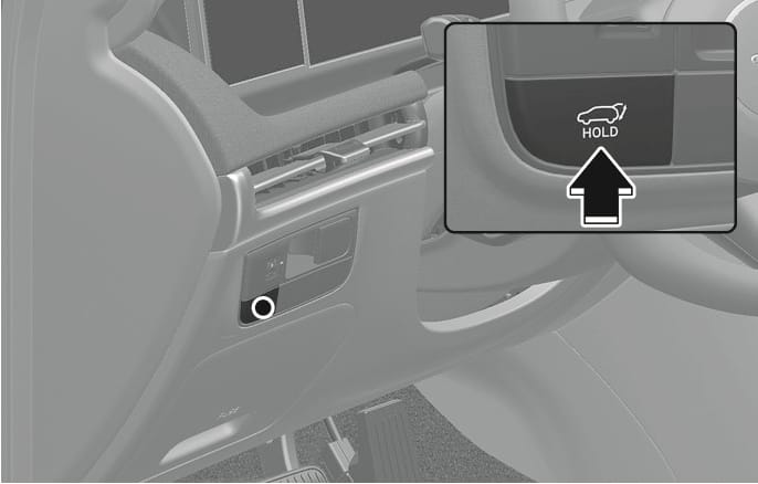 2025 Hyundai Tucson Power tailgate open/close button image. The image displays the button located on the driver's side crash pad. A detailed inset shows the button with a car icon with an open trunk and 'HOLD' text, indicated by a black arrow pointing upwards. Describes the function of opening or closing the power tailgate.