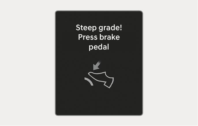 2025 Hyundai Tucson instrument cluster warning message image. The screen displays the text 'Steep grade! Press brake pedal' along with an icon of a foot pressing a pedal, indicated by a downward arrow. Explains the warning displayed on steep inclines to advise applying the brake to prevent transmission damage.