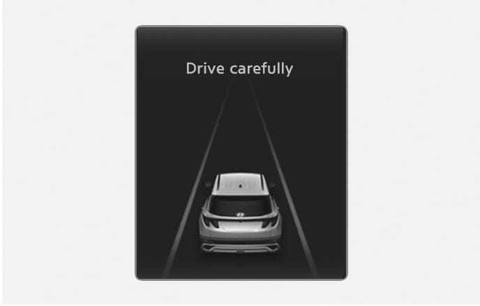 2025 Hyundai Tucson Forward Collision-Avoidance Assist warning message image. The instrument cluster display shows the text 'Drive carefully' above a graphic of a vehicle positioned between lane lines. It explains the notification that appears when the vehicle is stopped due to emergency braking.