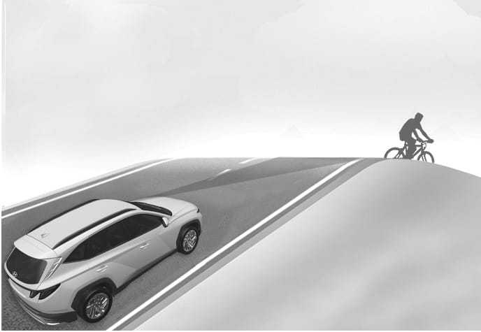 2025 Hyundai Tucson Forward Collision-Avoidance Assist limitation image. A white SUV drives up a steep hill with a cyclist just over the crest, obscured from the front camera's view. This illustrates the system's limitation in detecting objects on inclined roads.