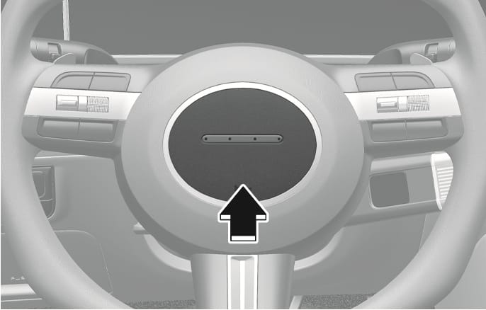2025 Hyundai Tucson steering wheel horn image. A black arrow points upward towards the center pad of the steering wheel, indicating the specific area to press. Explains the function of sounding the horn by pressing the designated area.