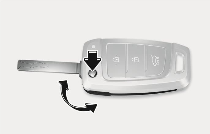 2025 Hyundai Tucson mechanical key image. A black vertical arrow points to the circular release button on the remote key, and a curved arrow indicates the movement of the key blade. Explains the function of pressing the release button to unfold or fold the mechanical key.