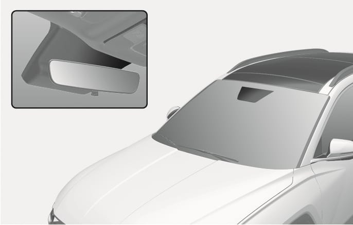 2025 Hyundai Tucson Auto defogging system sensor location image. The main view shows the vehicle's windshield with the sensor housing area at the top center. A detailed inset shows the interior rearview mirror and the sensor cover behind it. Describes the position of the sensor that automatically detects moisture to prevent fogging.