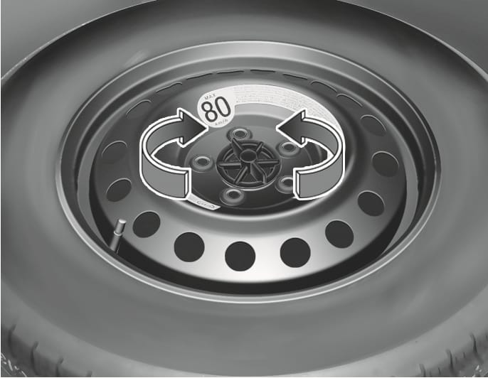 2025 Hyundai Tucson spare tire hold-down bolt image. Curved arrows indicate turning the central winged hold-down bolt counter-clockwise. A 'MAX 80 km/h' sticker is visible on the wheel. Explains the process of loosening the bolt to remove the spare tire.