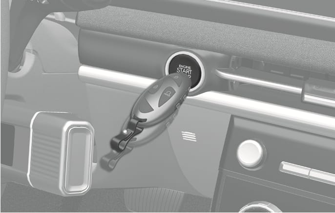 2025 Hyundai Tucson smart key emergency start image. A smart key fob is positioned to press the Engine Start/Stop button on the dashboard. Explains the method to start the engine by pushing the button with the smart key when the key battery is weak.
