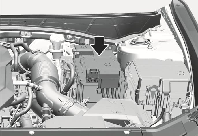 2025 Hyundai Tucson battery location image. A black arrow points downward to the battery unit situated in the engine compartment between the air intake hose and the fuse box. Explains the position of the battery for maintenance and inspection.