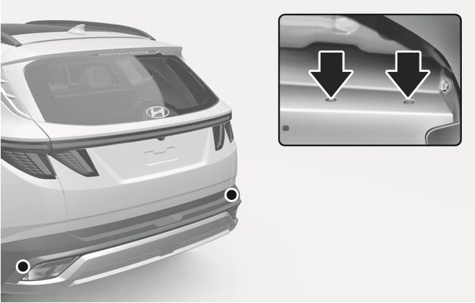 2025 Hyundai Tucson Trailer Hitch Mounting Locations image. The rear view highlights areas behind the rear tires, and an inset shows the underbody frame with two black arrows pointing downwards to the mounting holes. Explains the location of the mounting holes for hitches.