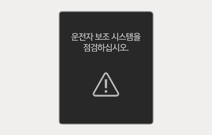 2025 현대 투싼 운전자 주의 경고 기능 이상 알림 화면 이미지입니다. 검은색 배경의 클러스터 화면에 '운전자 보조 시스템을 점검하십시오.'라는 흰색 문구와 삼각형 모양의 통합 경고등 아이콘이 표시되어 있습니다. 운전자 주의 경고 시스템에 이상이 감지되었을 때 운전자에게 점검 필요성을 알리는 기능을 설명합니다.