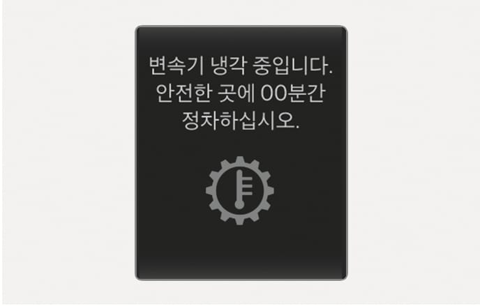 2025 현대 투싼 클러스터 경고문 이미지입니다. 화면에 '변속기 냉각 중입니다. 안전한 곳에 00분간 정차하십시오.' 문구와 톱니바퀴 속 온도계 아이콘이 표시되어 있습니다. 변속기 냉각을 위해 정차 후 대기해야 함을 알리는 화면 구성을 설명합니다.