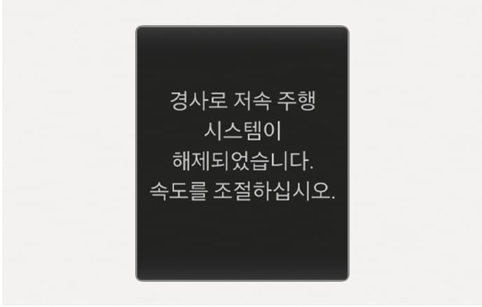 2025 현대 투싼 경사로 저속 주행 시스템 해제 알림 이미지입니다. 검은색 배경의 사각형 팝업 창 내부에 '경사로 저속 주행 시스템이 해제되었습니다. 속도를 조절하십시오.'라는 흰색 안내 문구가 표시되어 있습니다. 시스템 작동이 불가능한 상황에서 운전자에게 수동으로 속도를 조절하도록 경고하는 화면 구성을 설명합니다.