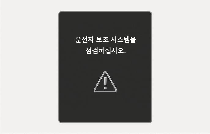 2025 현대 투싼 전방 충돌방지 보조 기능 이상 경고 화면 이미지입니다. 클러스터 화면 중앙에 '운전자 보조 시스템을 점검하십시오.'라는 흰색 문구와 그 아래에 삼각형 모양의 느낌표 경고 아이콘이 표시되어 있습니다. 전방 충돌방지 보조 시스템에 이상이 발생했을 때 운전자에게 점검이 필요함을 알리는 기능을 설명합니다.