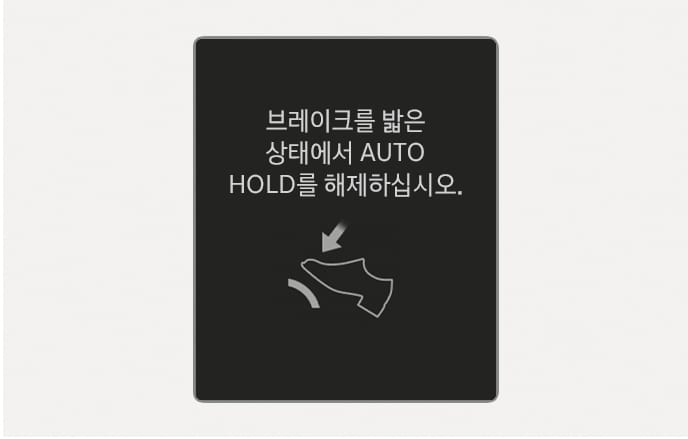 2025 현대 투싼 클러스터 표시창 경고문 이미지입니다. 검은색 배경 중앙에 '브레이크를 밟은 상태에서 AUTO HOLD를 해제하십시오.'라는 흰색 문구가 표시되어 있습니다. 하단에는 발로 브레이크 페달을 밟는 모습의 아이콘과 아래쪽을 가리키는 화살표가 있어 조작 방법을 안내합니다. 브레이크를 밟지 않고 자동 정차 기능을 해제하려 할 때 올바른 조작 방법을 안내하는 기능을 설명합니다.