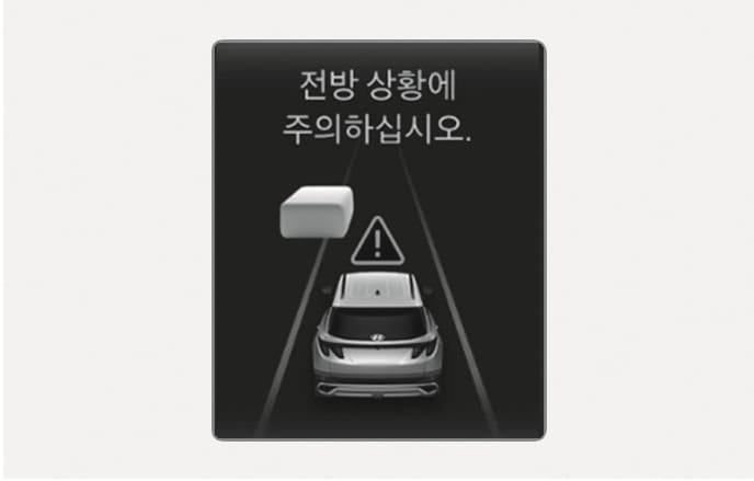 2025 현대 투싼 스마트 크루즈 컨트롤 전방 상황 주의 경고 화면 이미지입니다. 클러스터에 '전방 상황에 주의하십시오.' 문구와 함께 주행 차량, 전방 장애물 그래픽, 삼각형 느낌표 아이콘이 표시되어 있습니다. 주행 중 전방 주시가 필요한 상황임을 운전자에게 알리는 기능을 설명합니다.