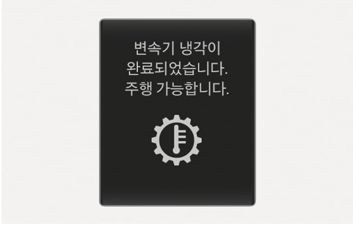 2025 현대 투싼 클러스터 표시창의 변속기 냉각 완료 안내 이미지입니다. 검은색 배경 화면 중앙에 톱니바퀴와 온도계가 결합된 아이콘이 있으며, 상단에 '변속기 냉각이 완료되었습니다. 주행 가능합니다.'라는 문구가 표시되어 있습니다. 변속기 과열 상태가 해소되어 정상적인 주행이 가능함을 운전자에게 알리는 기능을 설명합니다.