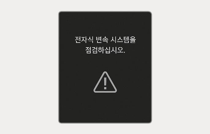 2025 현대 투싼 전자식 변속 시스템 점검 경고 이미지입니다. 검은색 배경의 클러스터 화면 중앙에 '전자식 변속 시스템을 점검하십시오.'라는 흰색 문구가 표시되어 있고, 그 아래에 삼각형 모양의 주의 경고 아이콘이 위치합니다. 변속 기능이 정상적으로 작동하지 않을 때 운전자에게 시스템 점검 필요성을 알리는 기능을 설명합니다.